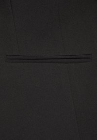 Czarna marynarka z tkaniny o eleganckim kroju, teksturowanym materiale i wąskiej, poziomej kieszeni po lewej stronie.