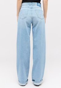 Light blue denim wide-leg jeans with a high waist, featuring two back pockets and a rolled hem. Soft texture with minimal stitching details.