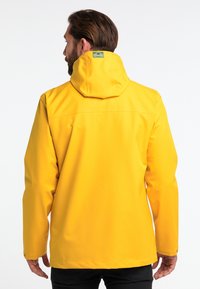 Chaqueta impermeable amarilla con capucha, con una textura suave, detalles de costura y una etiqueta de logo en el área del cuello.