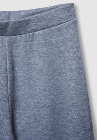 Ingrandimento di pantaloni in morbido tessuto blu-grigio melangiato che mostra i dettagli della vita e della cucitura laterale su uno sfondo chiaro.