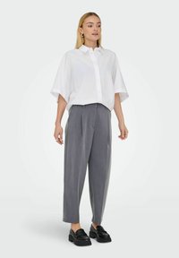 Bílá oversized košile s krátkými rukávy, spárovaná se šedými skládacími širokými kalhotami. Černé mokasíny dokončují tento outfit.