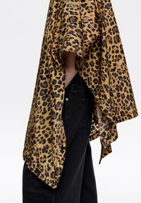 Top de estampado de leopardo con un diseño suelto y fluido, con una base dorada y manchas negras. La tela texturizada cae elegantemente sobre unos vaqueros oscuros.