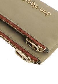 Bolsa de tela beige con cremalleras doradas dobles, acentos en color burdeos y logotipo grabado. Textura suave y diseño aerodinámico.