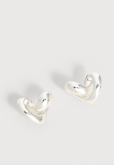 Ζευγάρι λαμπερών ασημένιων σκουλαρικιών σε σχήμα στεφάνης με ελικοειδές σχέδιο και λεία, γυαλιστερή επιφάνεια, σε απλό ανοιχτόφωτο φόντο.