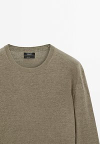 Pull en lin marron clair à manches longues avec col rond côtelé, montrant l'étiquette à l'intérieur de la zone du cou.