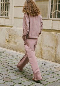 Różowa dżinsowa kurtka i dopasowane dzwony, oba z miękkiej tkaniny. Luźny krój, prosty styl, widoczne tylne kieszenie w spodniach.