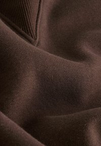 Brown knit fabric shows a soft, textured surface with a slight stretch. Features a ribbed neckline. The color is uniform and rich.