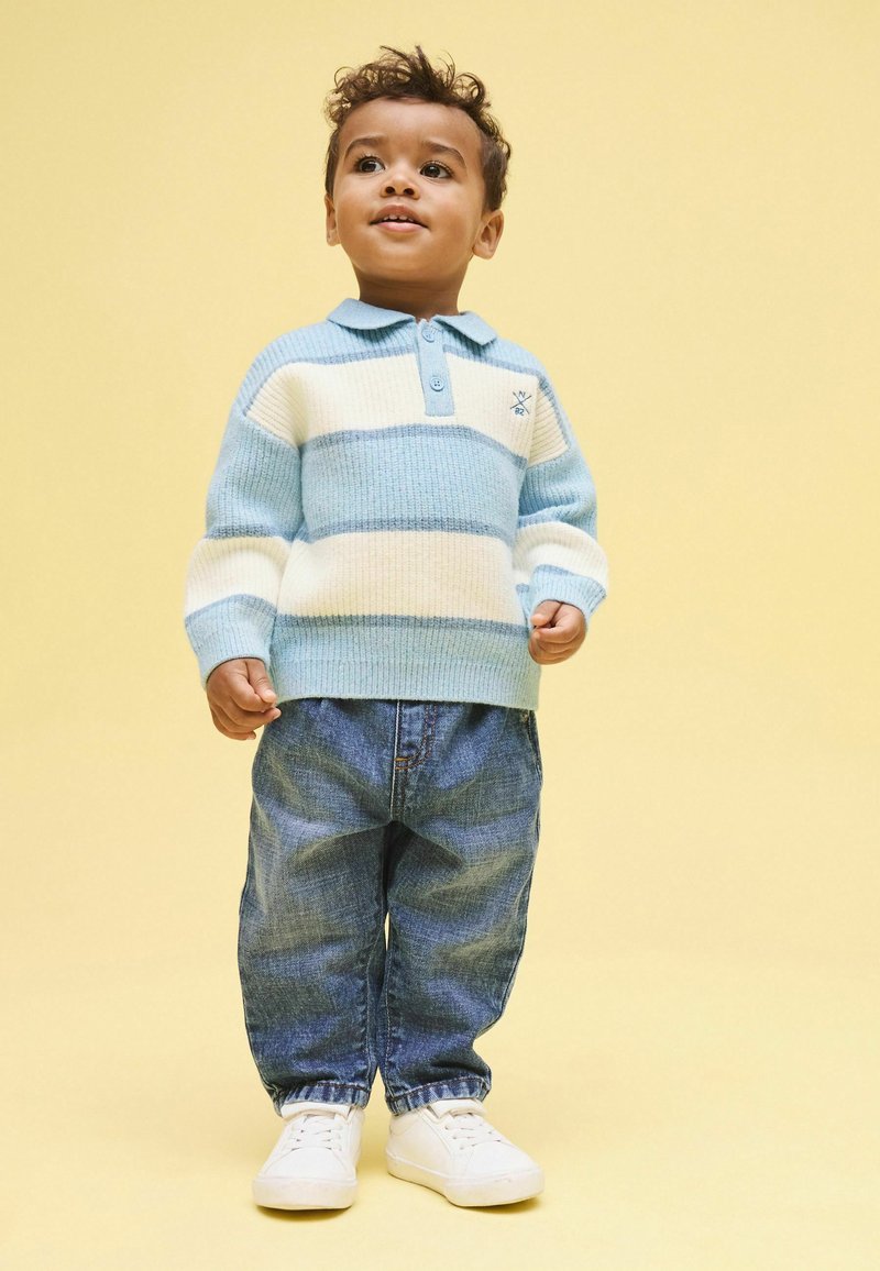 Vaaleansininen ja kerma raidallinen neulepaita kauluksella, yhdistetty väljästi istuviin farkkuihin ja valkoisiin kenkiin. Yksinkertainen, kodikas malli.