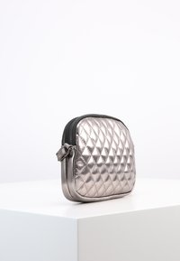 Borsa a cerniera trapuntata di colore argento metallico con bordi arrotondati e un anello laterale per l'attacco. Texture liscia con finitura lucida. Design compatto.