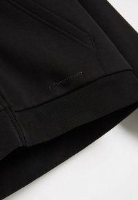 Czarny sportowy sweatshirt z ribbowanymi mankietami i gładką teksturą. Posiada srebrne logo na dolnym brzegu oraz kątowe detale szwów.