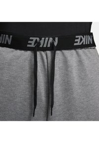 De grijze sweatpants van Nike hebben een zwarte elastische tailleband met een logo, zwarte trekkoorden en een zachte textuur. Close-up weergave van het taillegebied.