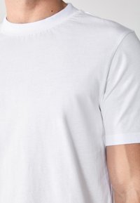 Bijela majica kratkih rukava s okruglim izrezom; napravljena od mekog pamučnog materijala; glatka tekstura; blago prilagođeni kroj.