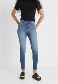 Jeans ajustados de color azul con un efecto desteñido, hechos de tela de mezclilla. Combinados con un top negro de canalé y sandalias de plataforma negras.