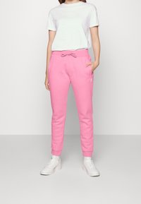 Rosa mjukisbyxor i mjukt material med dragsko i midjan och sidfickor, kombinerat med en enkel vit t-shirt och vita sneakers.