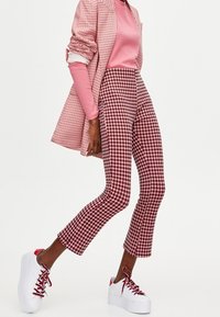 Czerwono-białe spodnie w kratę w jodełkę o krótkim kroju, zestawione z dopasowaną kratkowaną marynarką i różowym topem. Na nogach białe sneakersy na platformie.