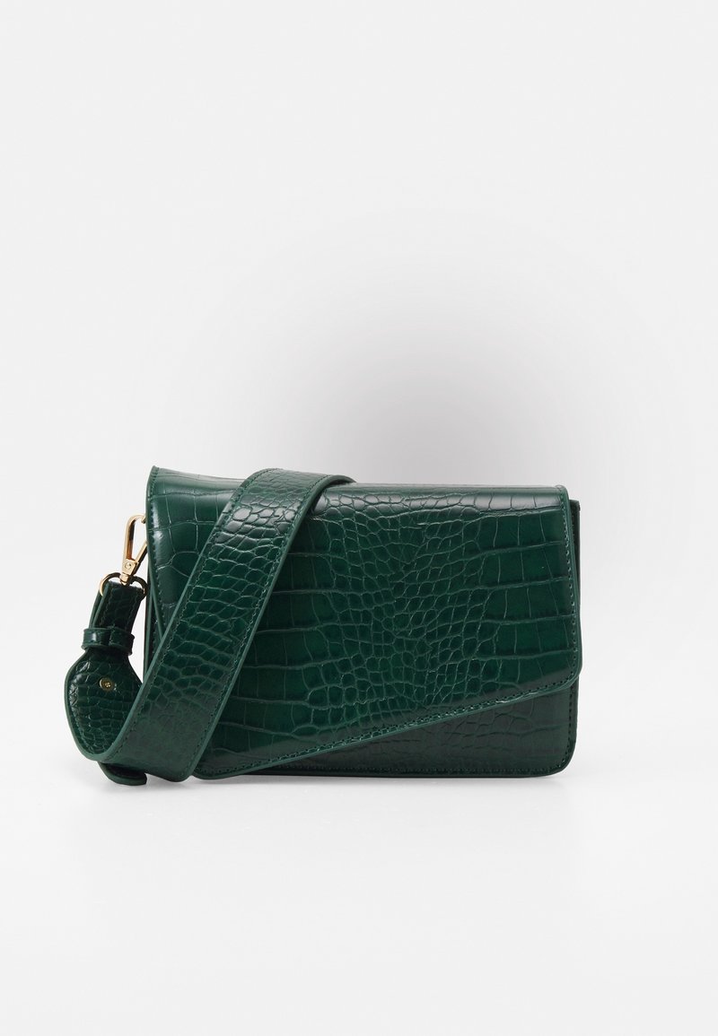 Mörkgrön texturerad handväska med en lång rem, med en elegant design och glänsande yta, uppställd mot en ljus bakgrund.