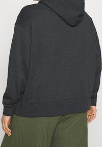 Mörkgrå hoodie med stor huva och ribbade ärmslut, tillverkad av mjukt material, med en avslappnad passform och standard fåll.