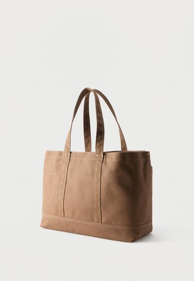 Sac fourre-tout en daim marron avec doubles bretelles, base rectangulaire et couture visible sur un fond clair uni.