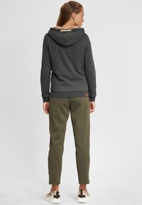 Hoodie gris foncé avec une capuche doublée en molleton beige, associé à un pantalon tapered vert olive et des baskets claires avec des accents marron.