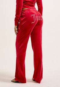 Rode fluwelen joggingbroek met een ontspannen pasvorm, voorzien van strass-bloemmotieven op de achterkant en een trekkoord in de taille voor verstelbaarheid.