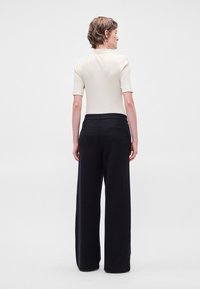 Ribota krēmkrāsas T-kreklis ar īsām piedurknēm apvienots ar plašām melnām strīpainām biksēm, kurām ir aizmugurējā kabata un teksturēts audums.