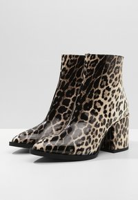 Stivaletti alla caviglia con stampa leopardata, finitura lucida, punta squadrata e tacco alto chunky. Il materiale è sintetico e presenta un audace motivo in bianco e nero.