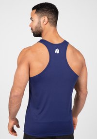 Marineblauwe sporttanktop van lichtgewicht materiaal, met een racerback ontwerp en een logo in het wit op de bovenrug bedrukt.