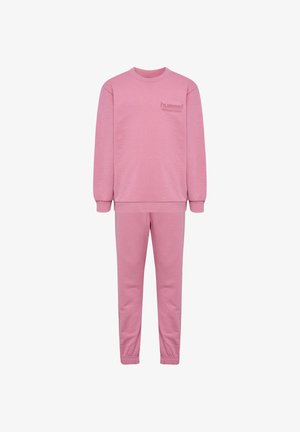 Zwei Kinder stehen da, tragen passende pinke Sweatshirts und Hosen, eines lächelt nach vorne, das andere schaut zur Seite.