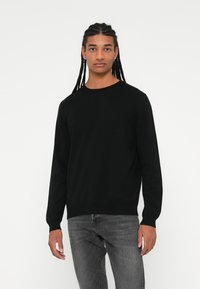 Zwarte gebreide trui met lange mouwen en een ronde halslijn, gecombineerd met grijze jeans. Gladde textuur en aansluitende silhouet. Minimalistisch ontwerp.