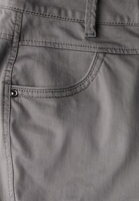 Le tissu gris du pantalon présente une poche avant avec un bouton-pression argenté, des coutures visibles et une texture lisse.