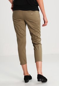 Khaki beskurna byxor med en figursydd design, med bakfickor och en jämn textur. Kombinerat med svarta ankelboots.