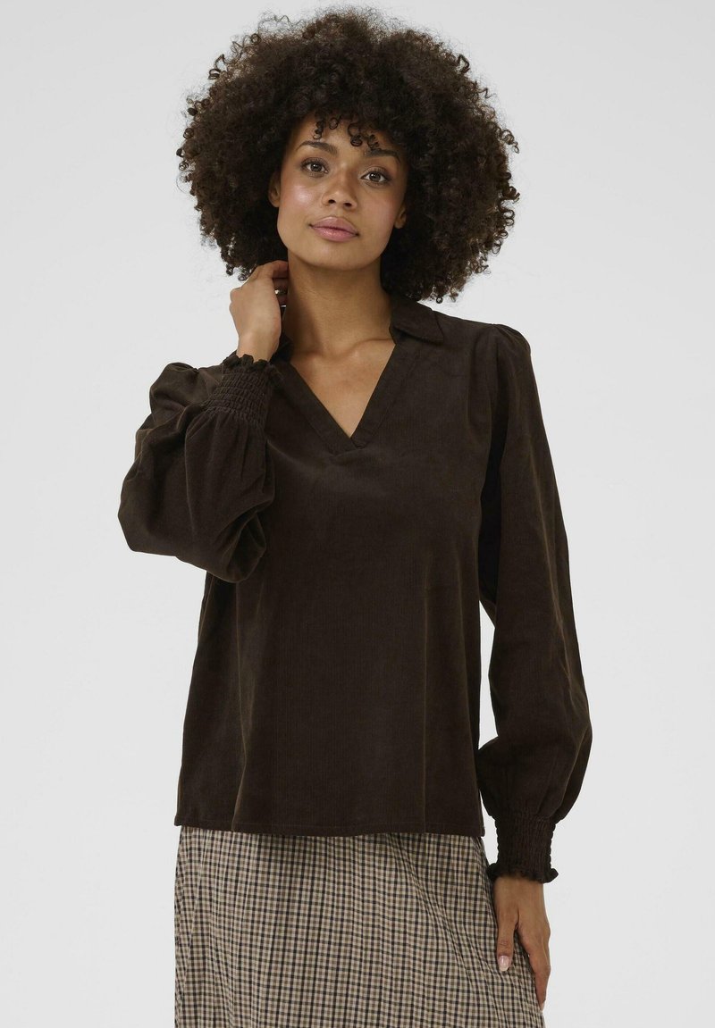Blouse en velours côtelé marron avec un décolleté en V, des manches bouffantes et des poignets smockés. Présente une texture lisse et une coupe décontractée.