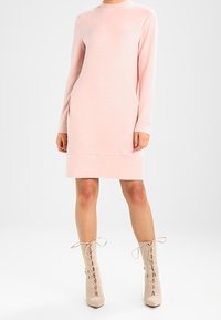 Abito maglione rosa a maniche lunghe con scollo rotondo e tasche laterali; abbinato a stivaletti alla caviglia beige chiaro con lacci. Texture liscia.