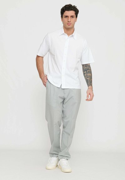 Camicia bianca a maniche corte con bottoni e colletto, abbinata a pantaloni grigi chiari e sneaker bianche, con una texture sottile.