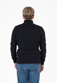 Maglione nero lavorato a maglia con colletto alto, polsini e vita a costine. Tessuto leggermente texturizzato. Indossato con jeans in denim blu.