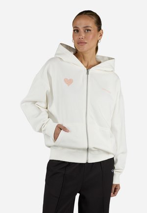 Witte zip-up hoodie van zacht stof, met een hartlogo aan de voorkant in lichtroze en kangoeroezakken. Ontspannen, oversized pasvorm.