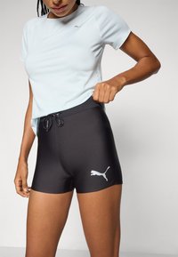 T-shirt de sport bleu clair à manches courtes et short noir ajusté avec un logo Puma blanc sur la jambe, détail de tissu texturé.