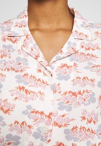 Short-sleeve floral shirt featuring a white base with pink, orange, and purple patterns, a notched collar, and a single button closure.
