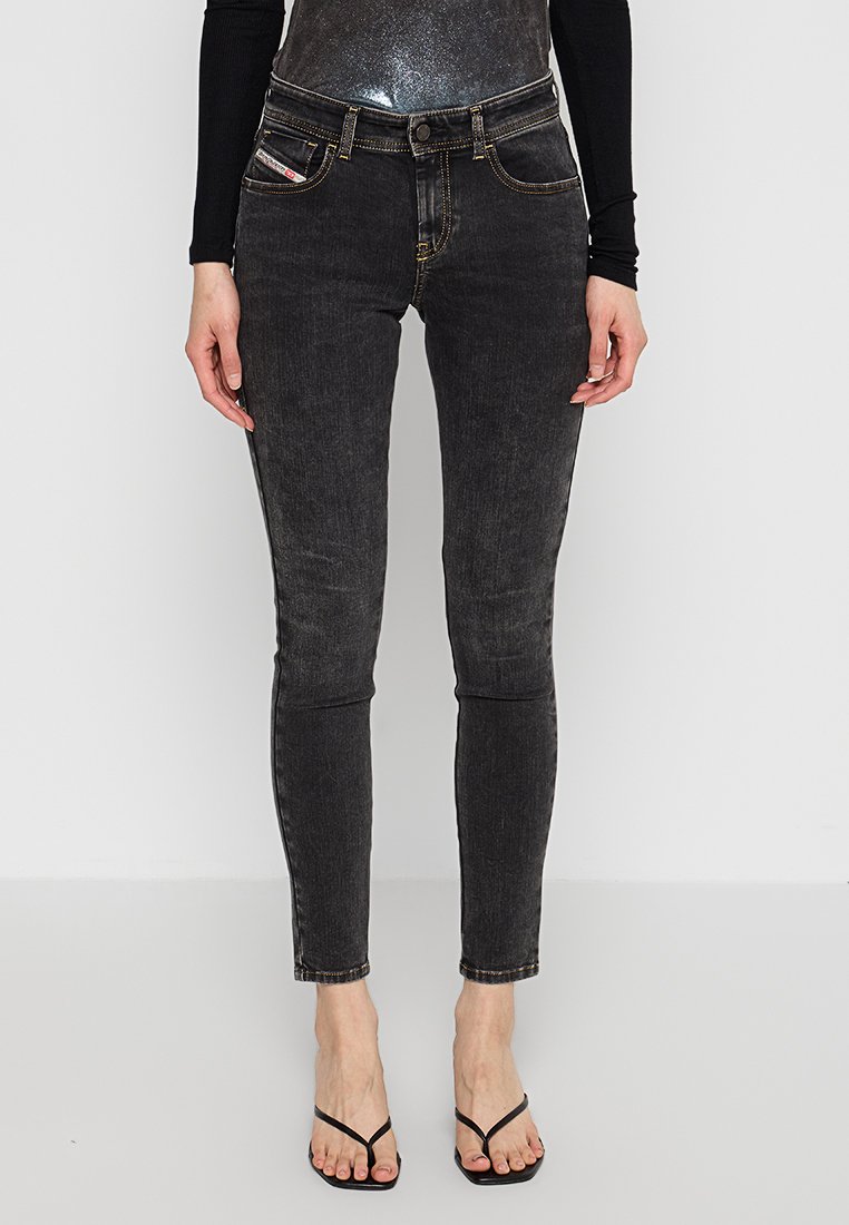 Jeans skinny neri con una texture sbiadita, caratterizzati da cinque tasche e cuciture gialle. Abbinati a un top nero aderente e sandali minimalisti.