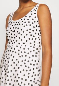 Puku dot -mekko, jossa on vaaleanpunainen kangas mustilla pisteillä, hihaton malli ja kapea vyötärö. Silkkinen pinta ja hienovarainen kiilto.