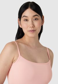 Jasnoróżowy, dopasowany top na ramiączkach z cienkimi paskami i gładką teksturą, podkreślający prosty, minimalistyczny design.