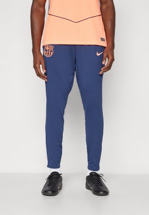 Atletika obleka s temo Barcelone, z oranžno majico in mornarsko modrimi hlačami. Hlače imajo logotip, so slim fit in so narejene iz lahkega blaga.