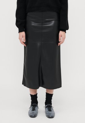 Czarna skórzana spódnica midi o dopasowanym kroju, gładkiej fakturze i pionowej szwie biegnącym przez środek. Podkreślona szarymi butami.