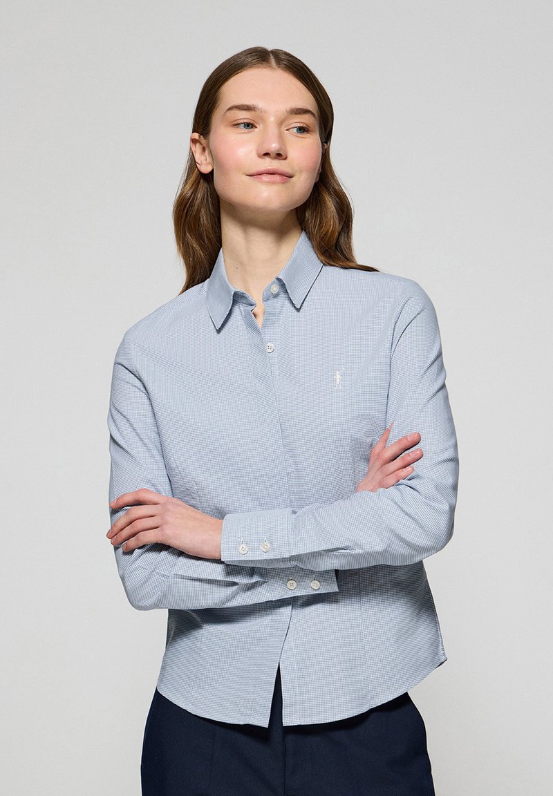 Camicia button-up azzurro chiaro con un leggero motivo a quadretti, colletto a punta e maniche lunghe con polsini abbottonati. Dettaglio del logo discreto sul petto.