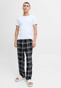 T-shirt bianco a collo rotondo abbinato a pantaloni da pigiama a quadri neri e beige, con una texture morbida e una vestibilità rilassata. Infradito bianche.
