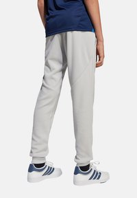 Helle graue Sporthose mit strukturiertem Stoff, tapered Beinen, Seitentaschen und einem blauen Akzent. Kombiniert mit weißen und blauen Turnschuhen.