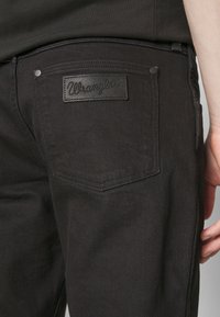 Jeans in denim nero con tasca posteriore dotata di etichetta in pelle testurizzata Wrangler e cuciture a contrasto. Progettati con una vestibilità slim.