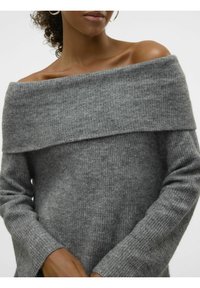Femme portant un pull en maille côtelée gris à manches longues, tombant sur les épaules, dévoilant ses clavicules et des boucles d'oreilles anneaux.