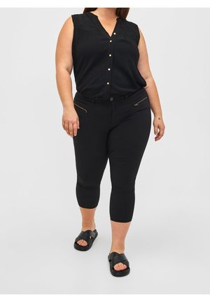 Sorte ærmeløs bluse med guldknapper og plisseret design, parret med sorte capri-bukser med lynlåslommer og en glat overflade. Sorte sandaler.