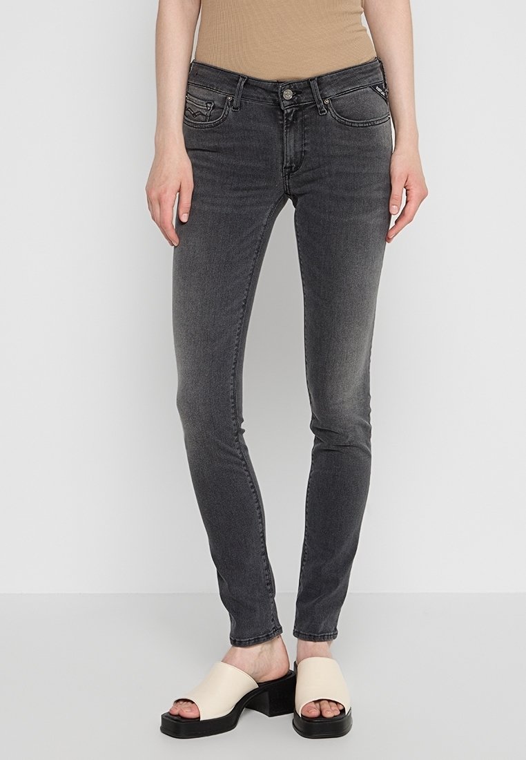 Jeans ajustados grises con un acabado ligeramente desgastado, cinco bolsillos y cierre de botón. Combinados con sandalias gruesas de color claro.